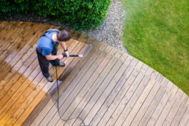 man cleaning terrace with a power washer - high water pressure cleaner on wooden terrace surface